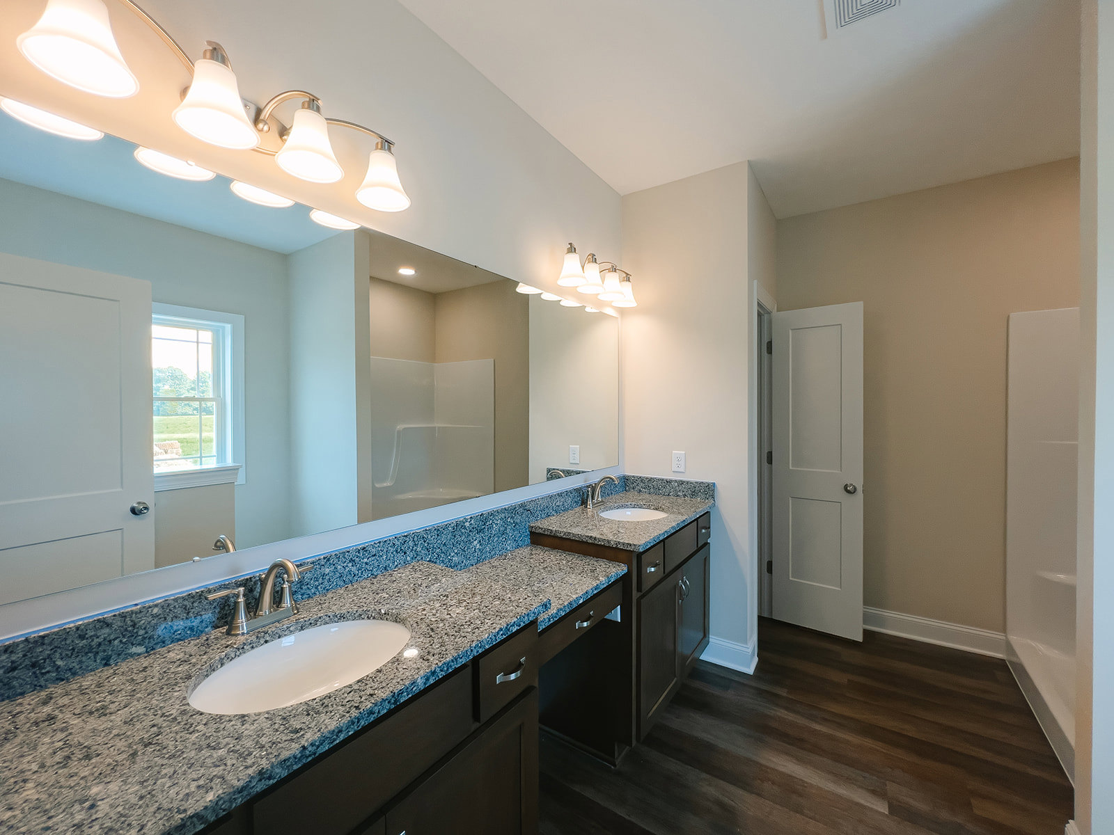Bathroom with marble countertops, large wall mirror, white oval sink, silver faucet, white cabinetry, window overlooking grassy field, silver door knob, illuminated light fixture