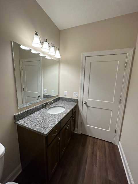 Modern bathroom featuring a wide mirror above a quartz countertop with undermount sink, sleek chrome faucet, white cabinetry, wall-mounted light fixtures, and neutral tile