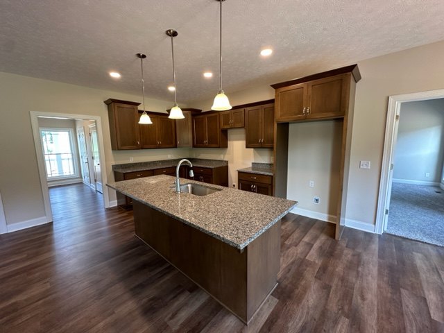 Spacious kitchen featuring a large central island with built-in sink, white cabinetry, hardwood flooring, stone countertops, and recessed lighting