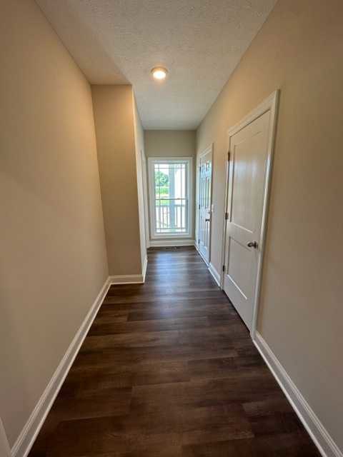 Hallway with dark wood flooring, white baseboards, two white doors with silver doorknobs, and a window with a white frame