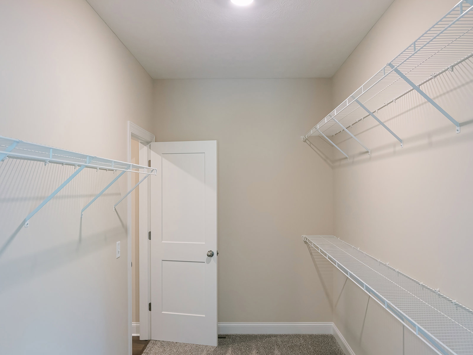 Walk-in closet with built-in white shelves, hanging clothes rack, and white door featuring a silver knob