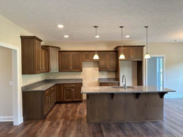Spacious kitchen featuring a large central island with built-in sink, white cabinetry, stone countertops, and wood flooring