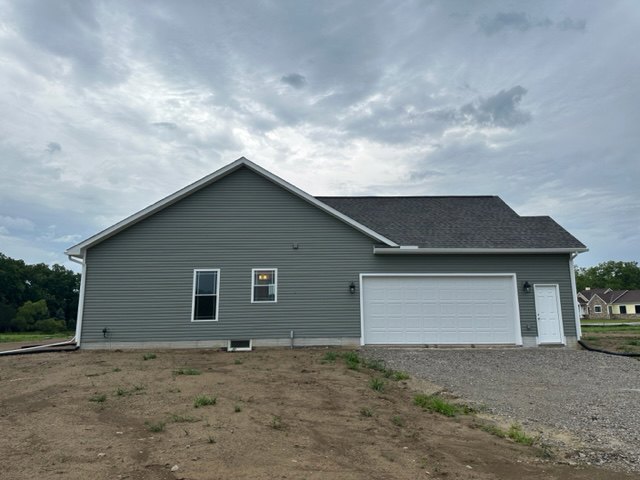 Two-story home with white siding and black trim, attached garage door, concrete driveway, grassy dirt hill, and overcast sky.