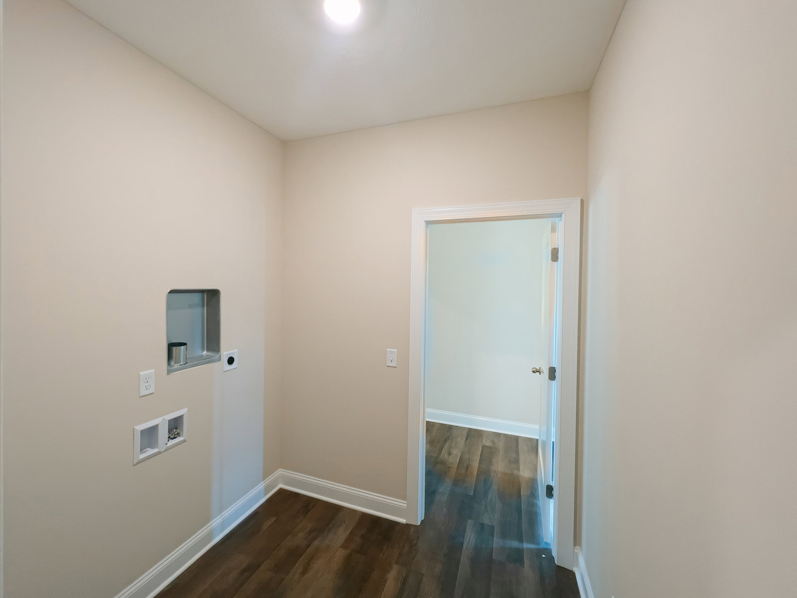 Wood plank flooring with white baseboard trim, white plaster walls, a single door, and a wall outlet; silver can on a shelf, ceiling with recessed lighting.