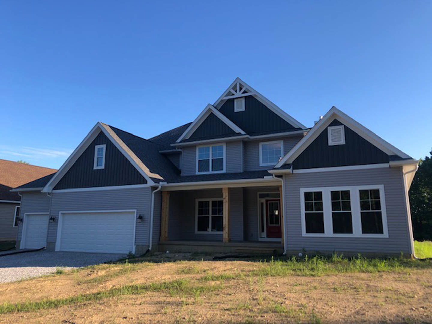 White brick house with black roof, attached garage, manicured green lawn, row of large windows with white frames, blue sky overhead