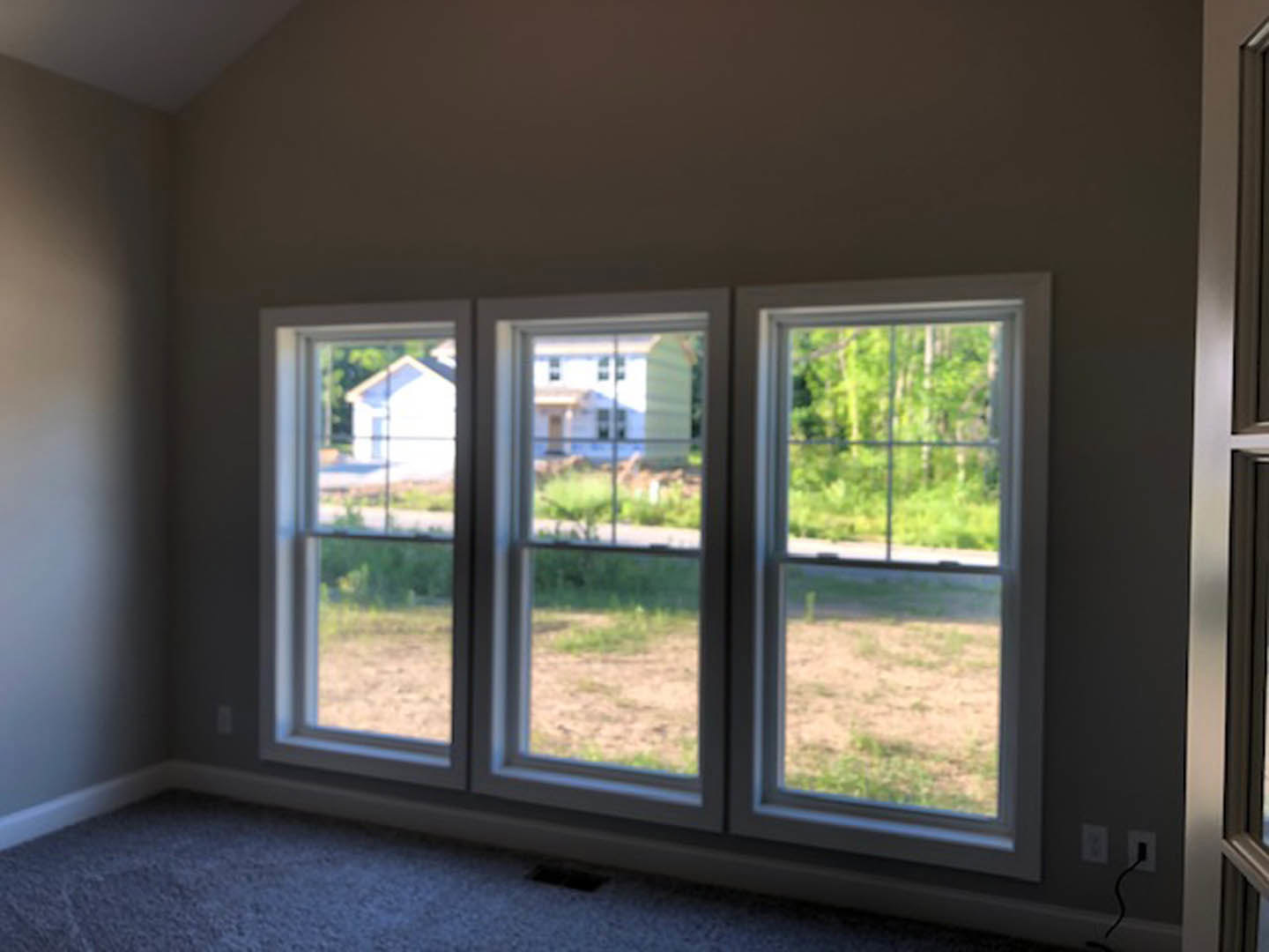 Bright room featuring large windows with views of green grass and trees outside, light-colored walls, hardwood flooring, and a ceiling vent.