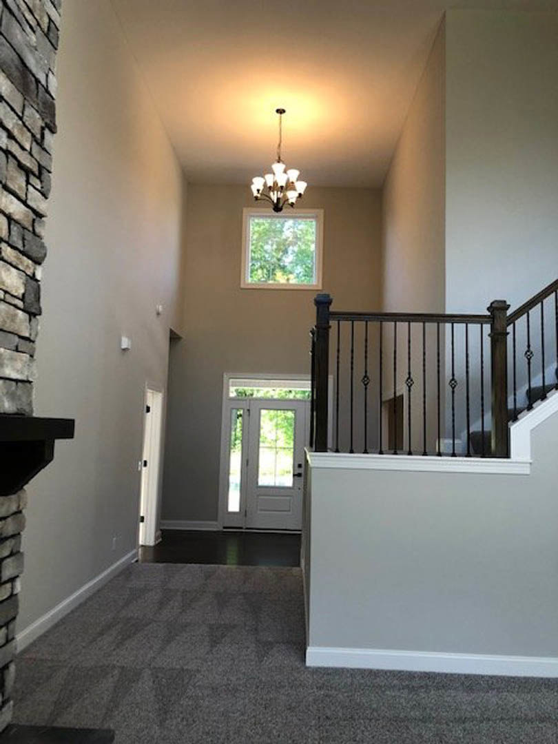 Hallway featuring a staircase with black railing, white door with glass panes, carpeted steps, light fixture near window, and plaster walls
