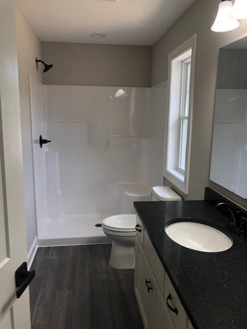 Modern bathroom featuring a black countertop with a white oval sink, wall-mounted faucet, tiled shower enclosure, and white toilet adjacent to the vanity.