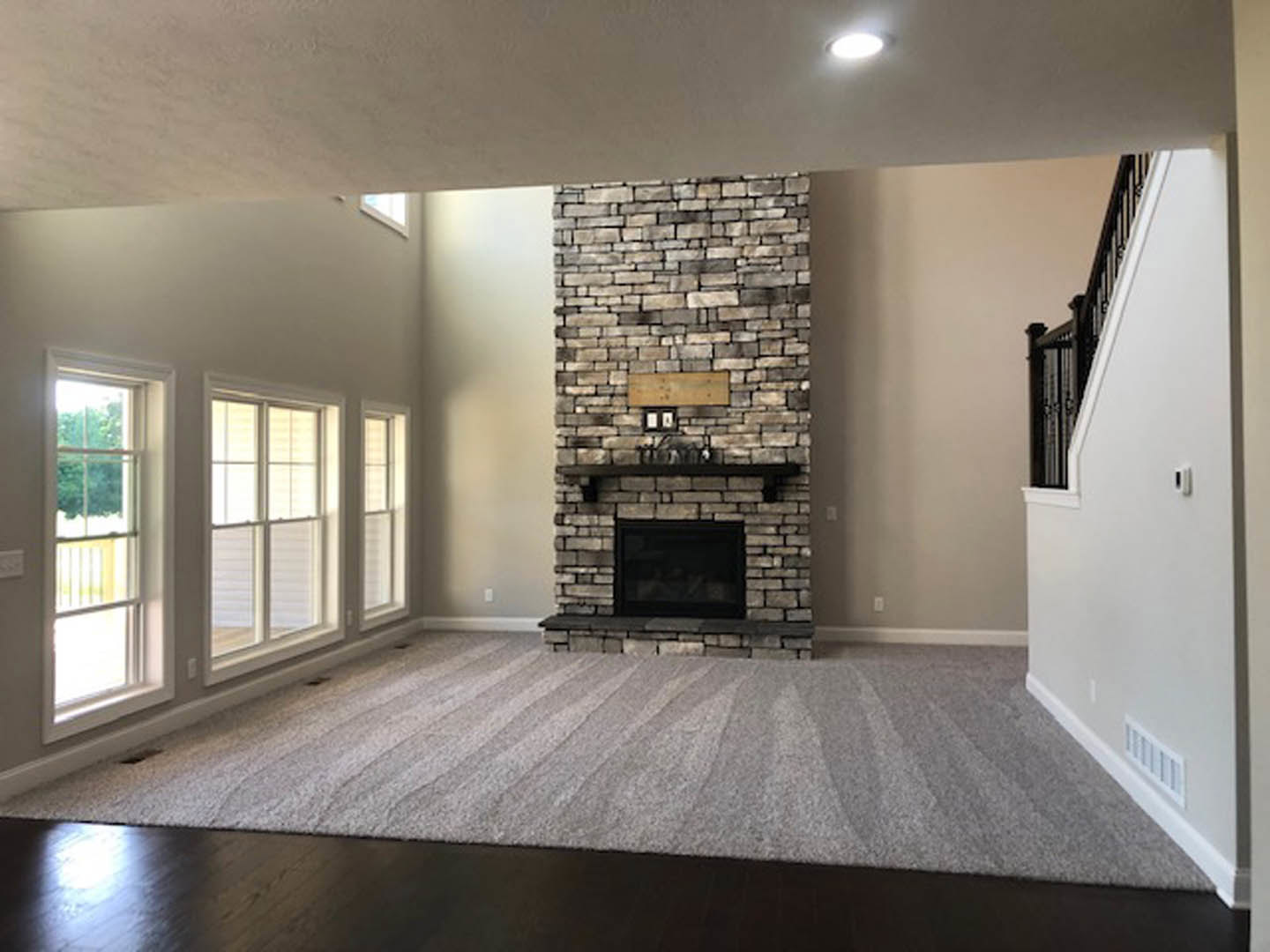 Carpeted living room with brick fireplace, wood mantel, white-framed window, and white walls.