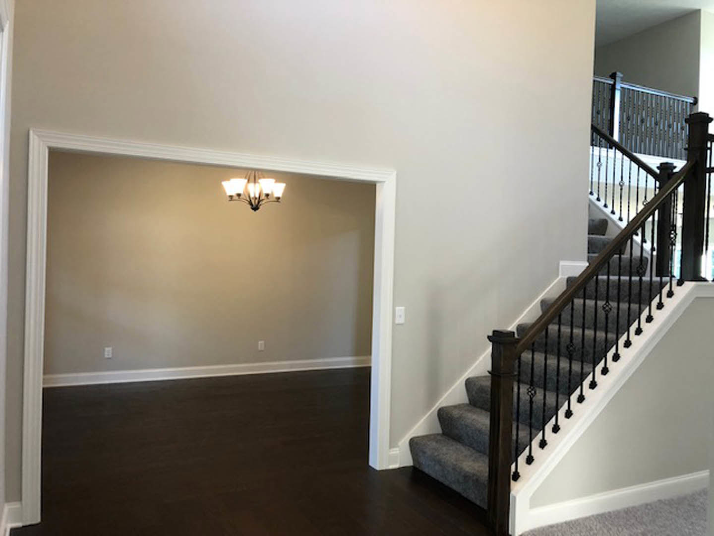 Wood staircase with black metal railings, light fixture overhead, neutral plaster walls, carpeted floor, and white ceiling.