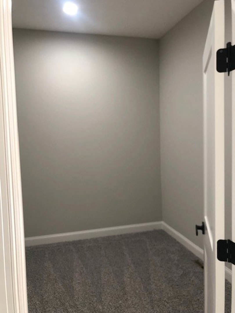 White-painted room with open door, plush beige carpet flooring, smooth plaster walls, and ceiling illuminated by recessed lighting.