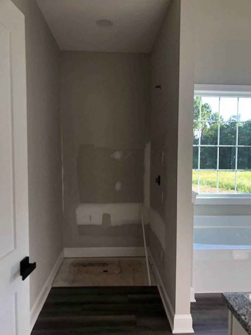 Bathroom with freestanding white tub, tiled floor and walls, window with metal bars, wooden door, and partial view of countertop and staircase.