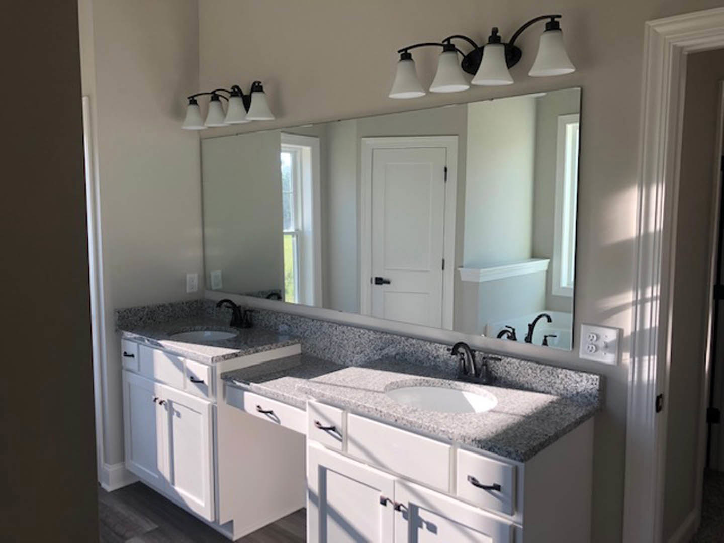 Bathroom featuring double sinks set in a stone countertop, expansive wall mirror above, white cabinetry with drawers, chrome faucets, and two modern white light fixtures mounted