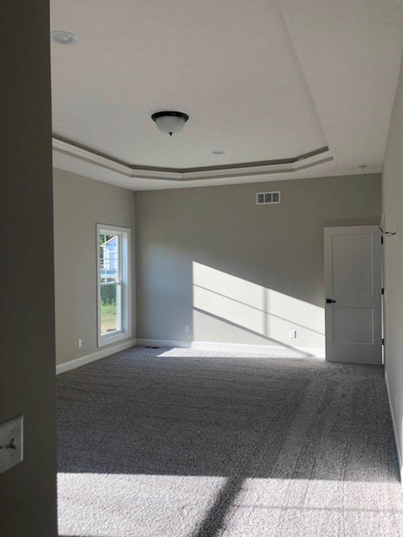 White paneled door with black handles, large window showing neighboring building, beige carpeted floor, wall-mounted clock, ceiling light fixture, smooth plaster walls and ceiling