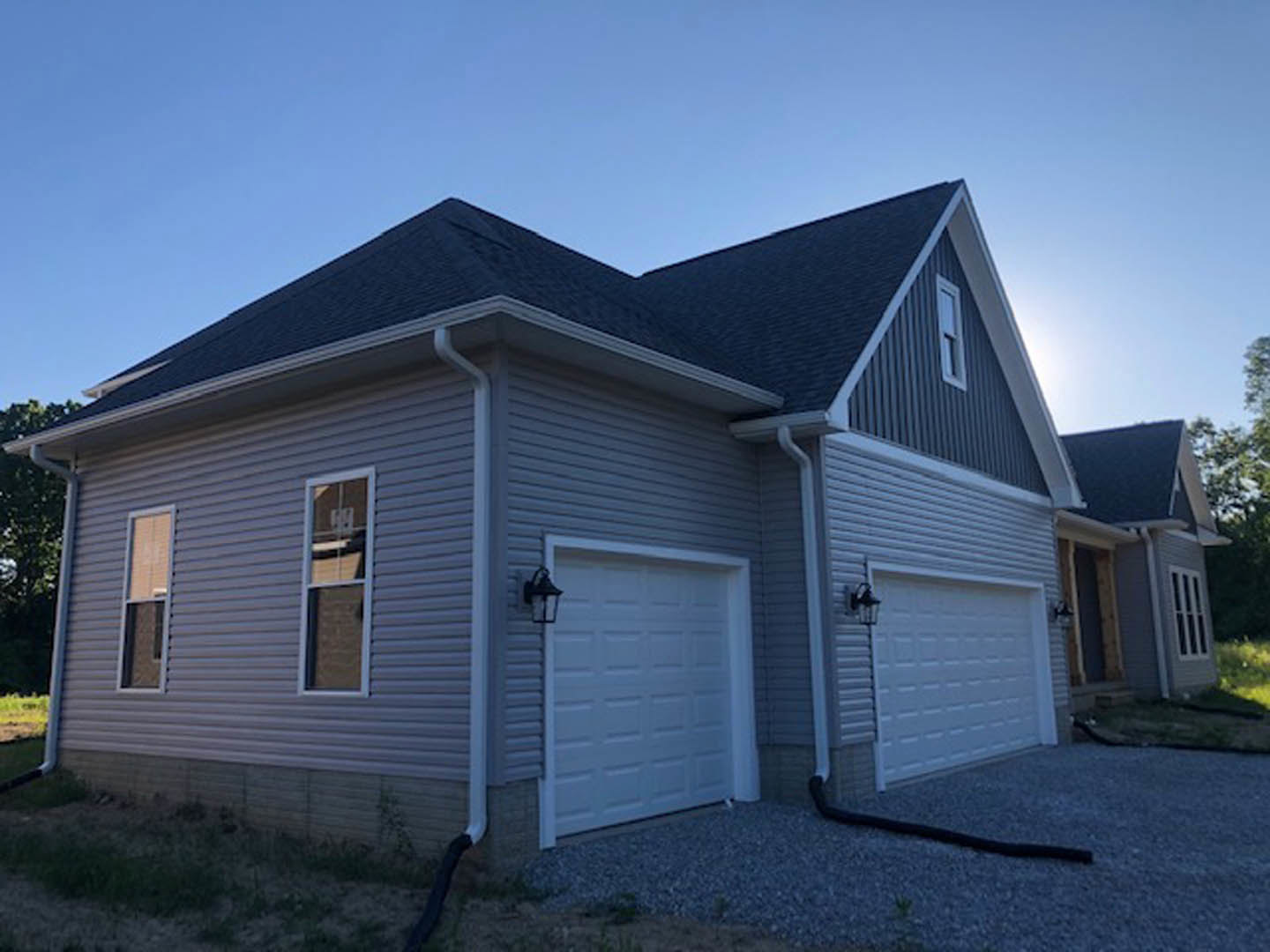 White garage door with side lamp, blue-trimmed window above, light-colored siding, gable roof, clear sky