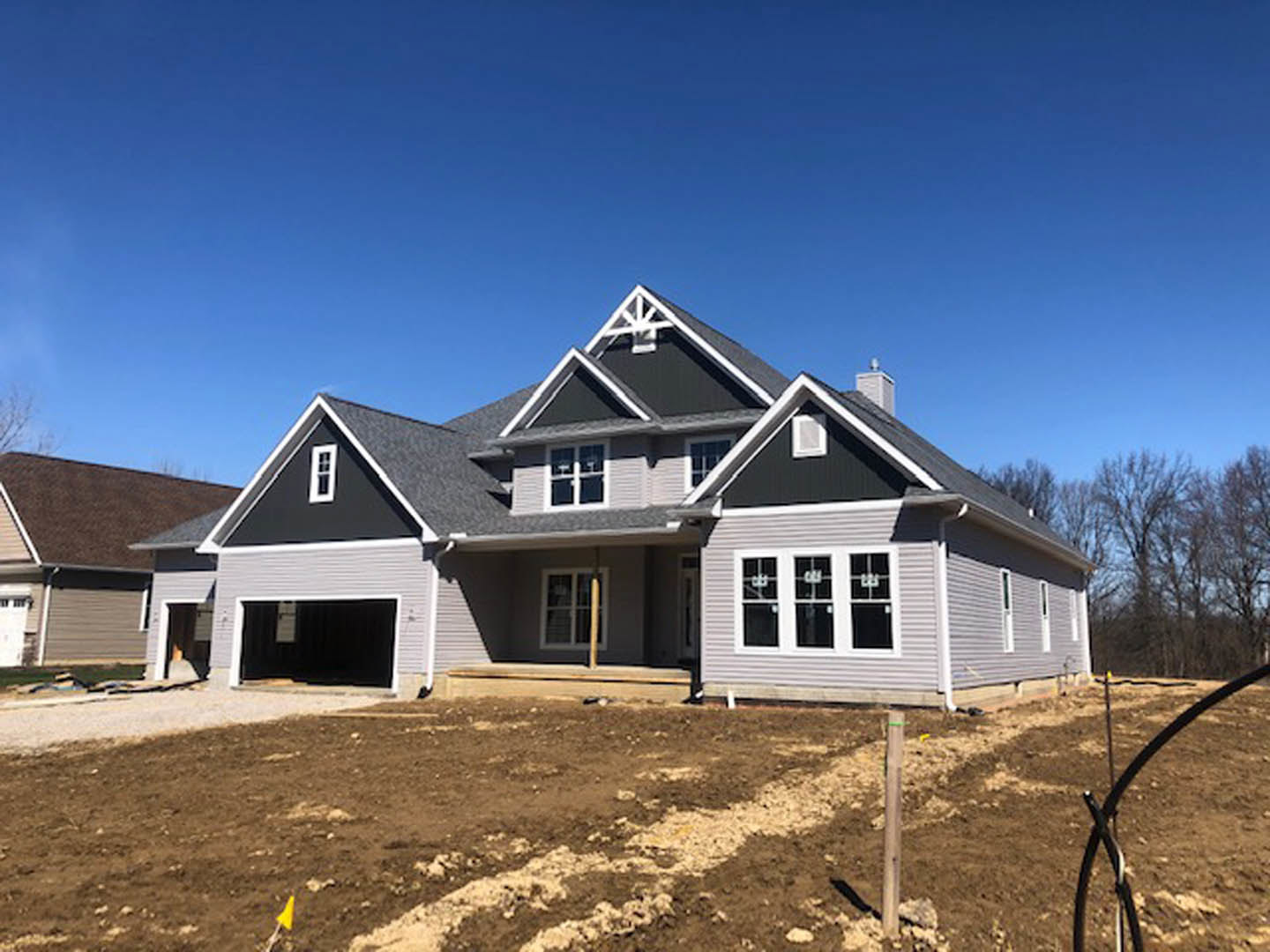 Partially built house with exposed framing, white window frames, unfinished porch, dirt lot, and surrounding trees