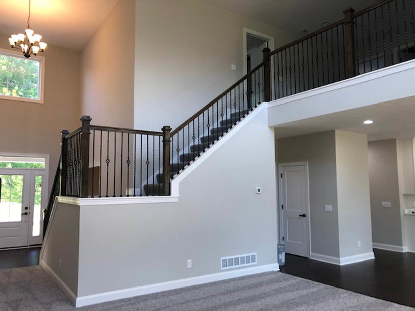 Wood staircase with white risers and black handrail, white paneled doors with black handles, window with modern light fixture, close-up of glass chandelier, grey carpet flooring