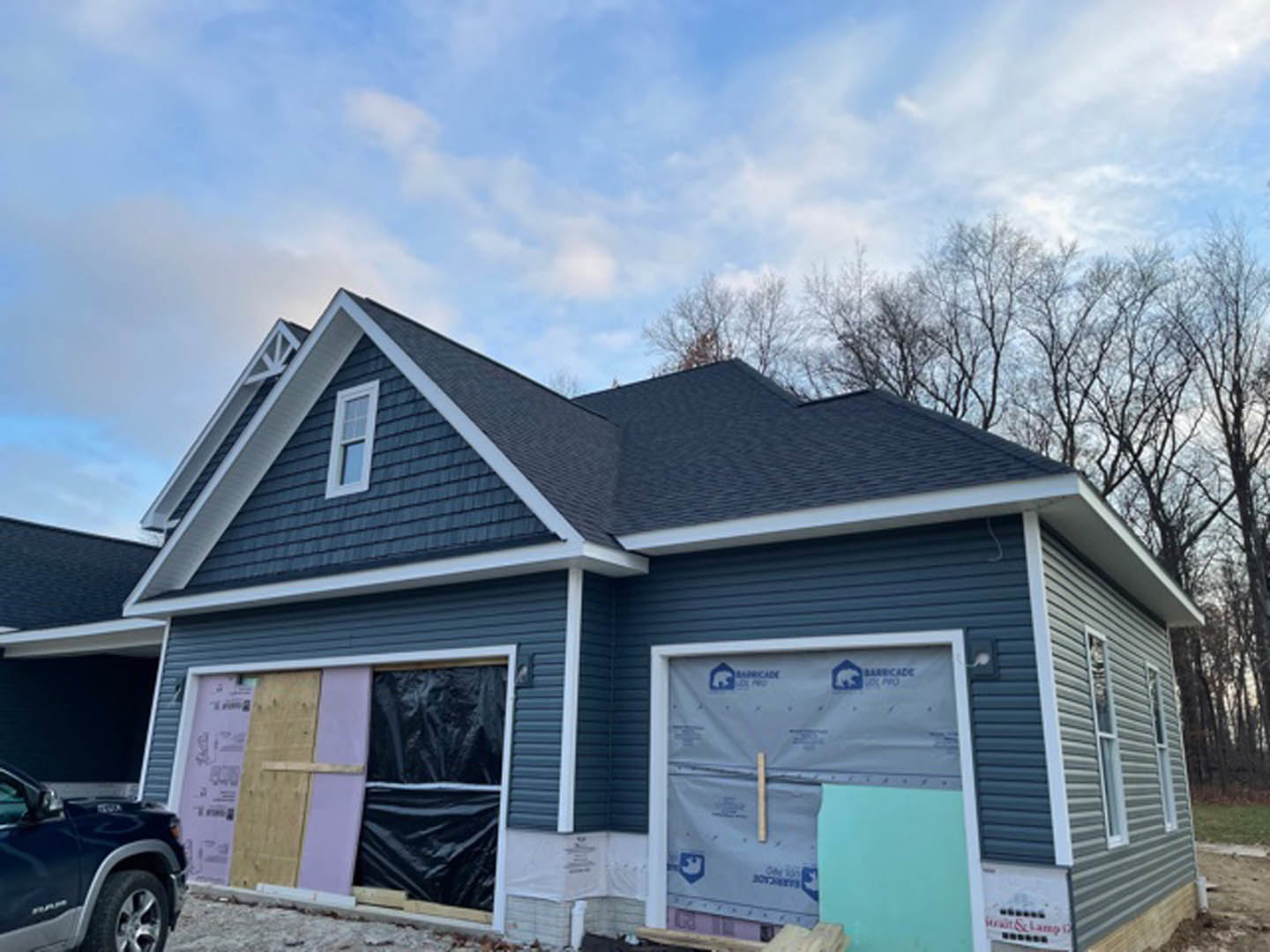 Modern home under construction featuring exposed framing, unfinished blue exterior walls, garage door, large windows, and a parked car in the driveway