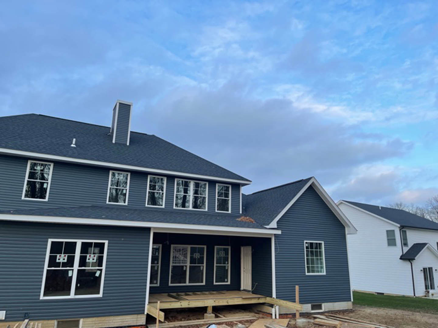 White siding house under construction with blue roof, white framed window, wooden pallet and metal rod on porch, clear blue sky overhead