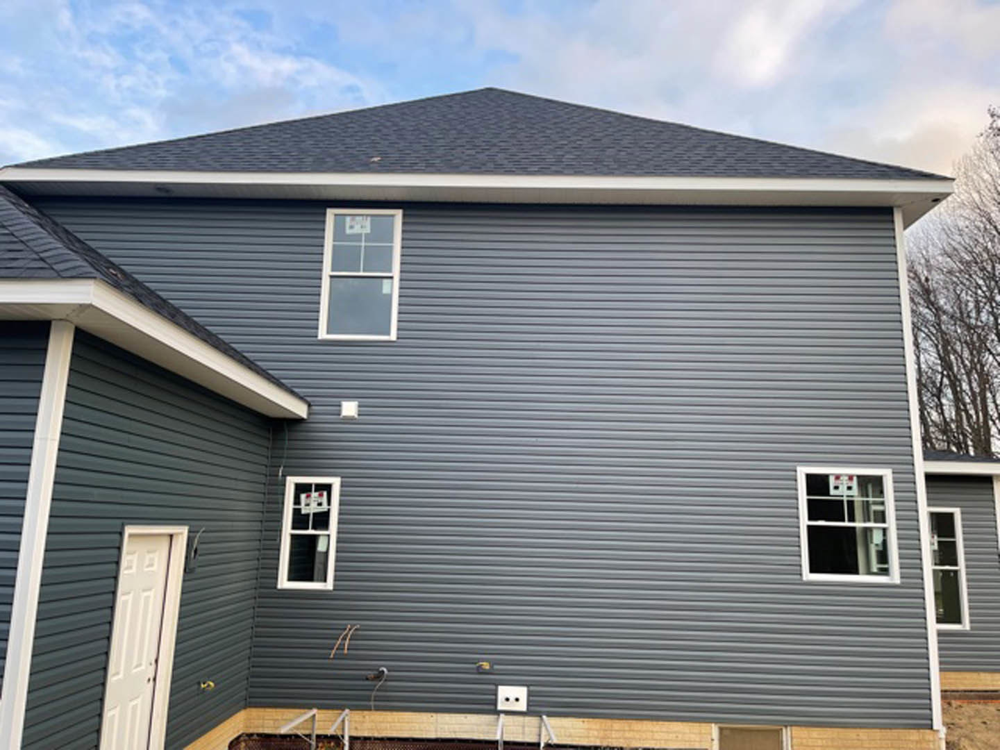 Blue siding house with white framed windows and white front door, small porch, basketball hoop visible through window, tree in foreground.