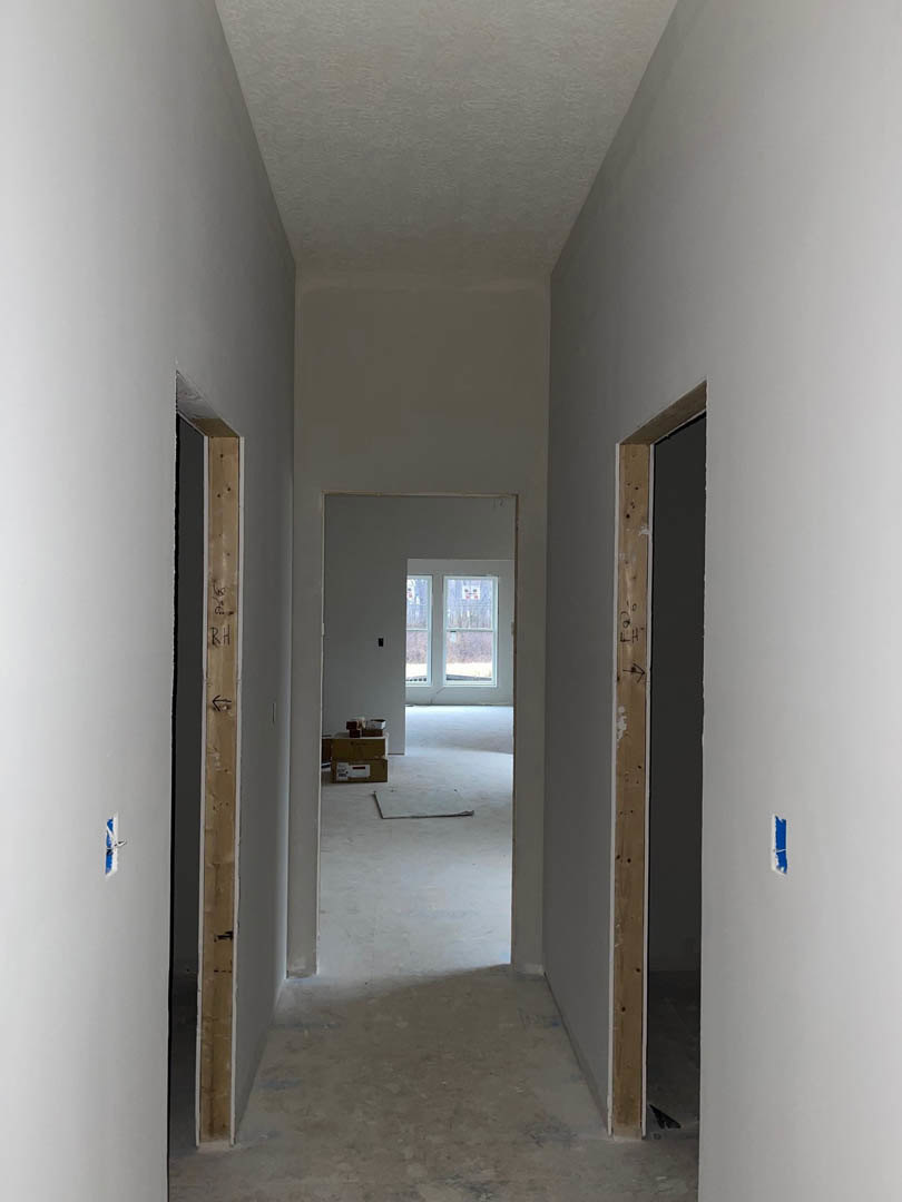 Hallway with smooth white plaster walls, light concrete flooring, a closed white door, and cardboard boxes stacked near the entrance