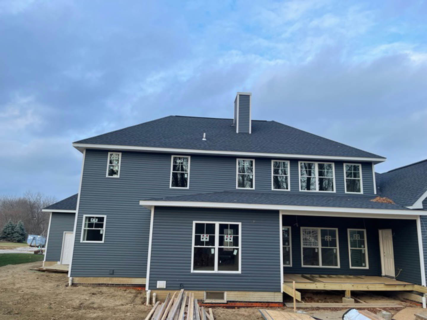 Partially built house with exposed wooden framing, white window frame with stickers, stack of wood planks, pallet in foreground, blue sky overhead