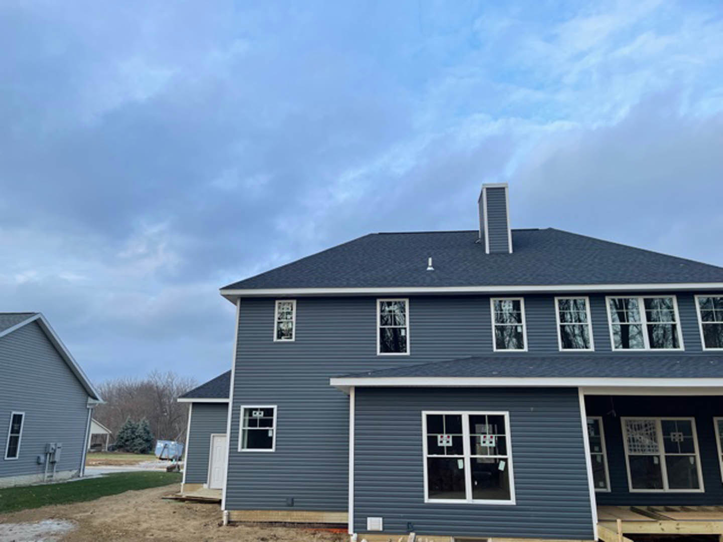 Grey siding house under construction with white roof, chimney, multiple windows featuring white frames and red dots, set against a clear blue sky