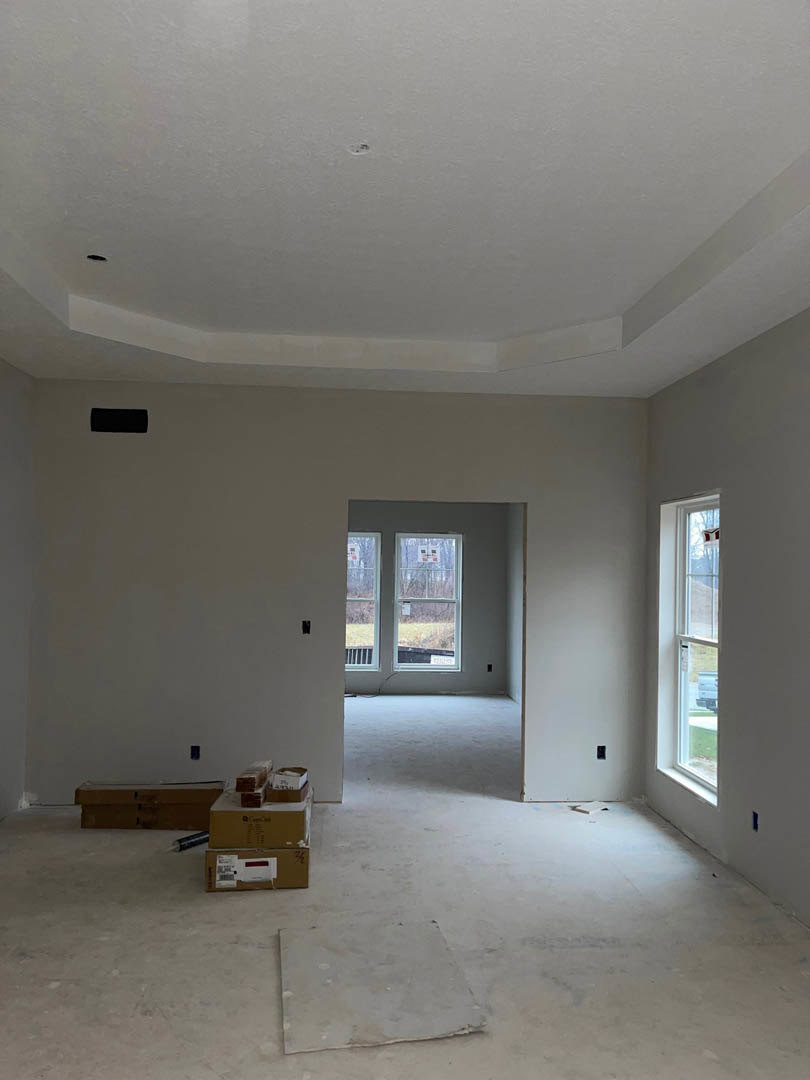 White-walled room with white ceiling featuring a hole, concrete floor, window with white frame, and stacked cardboard boxes