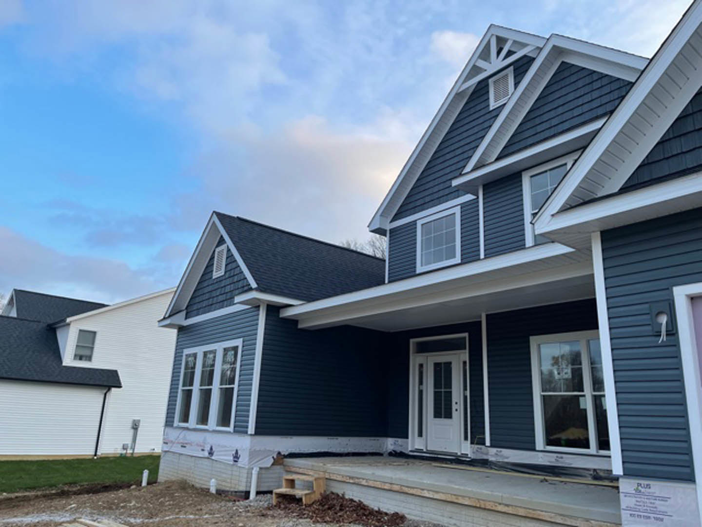 Blue siding exterior with white framed windows, white door featuring glass panes, and a white vent above the porch under a cloudy sky