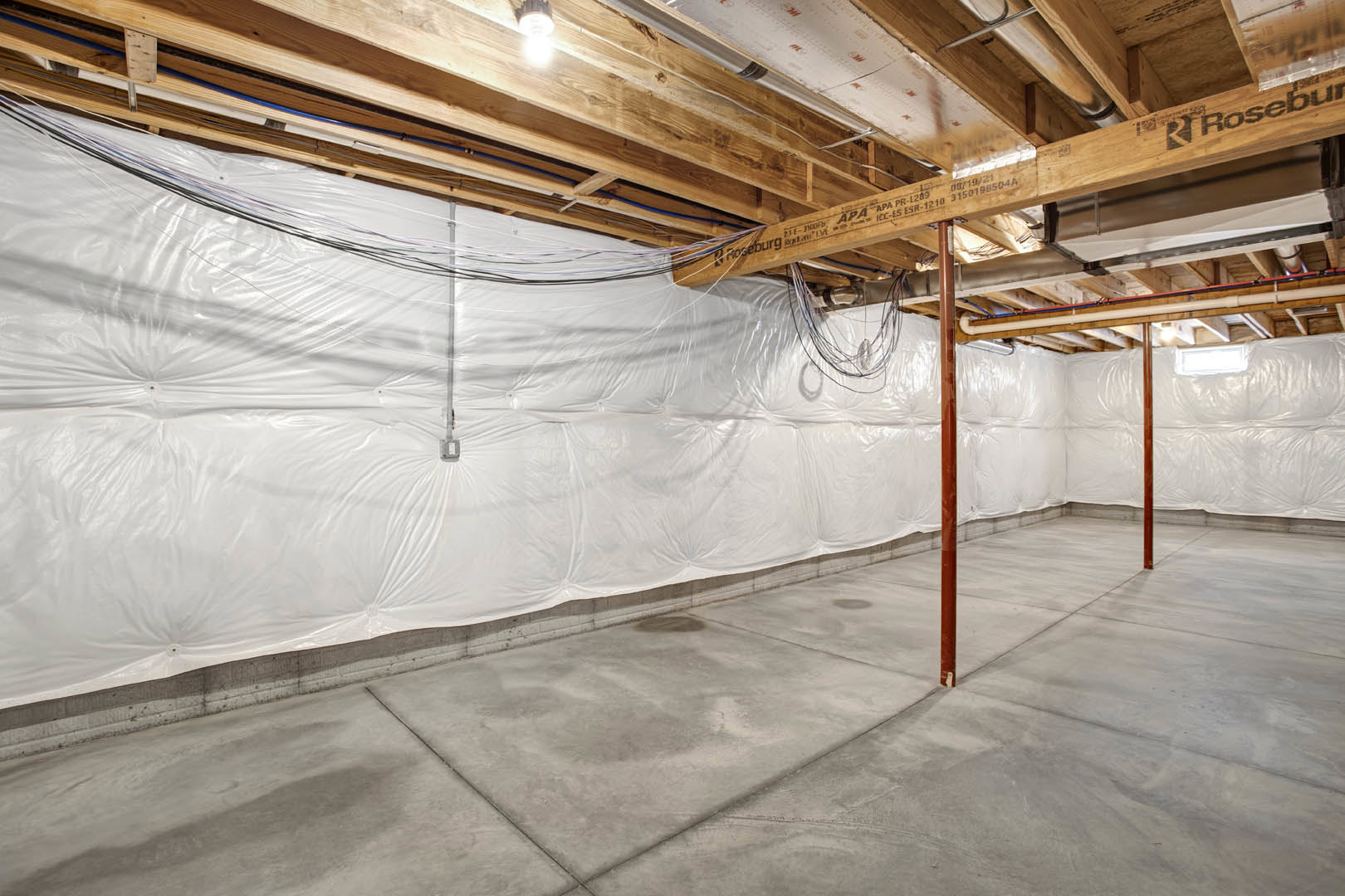White wall and ceiling with exposed wooden beams, concrete floor partially covered in white, visible electrical wiring along beams, close-up of a sign in foreground.