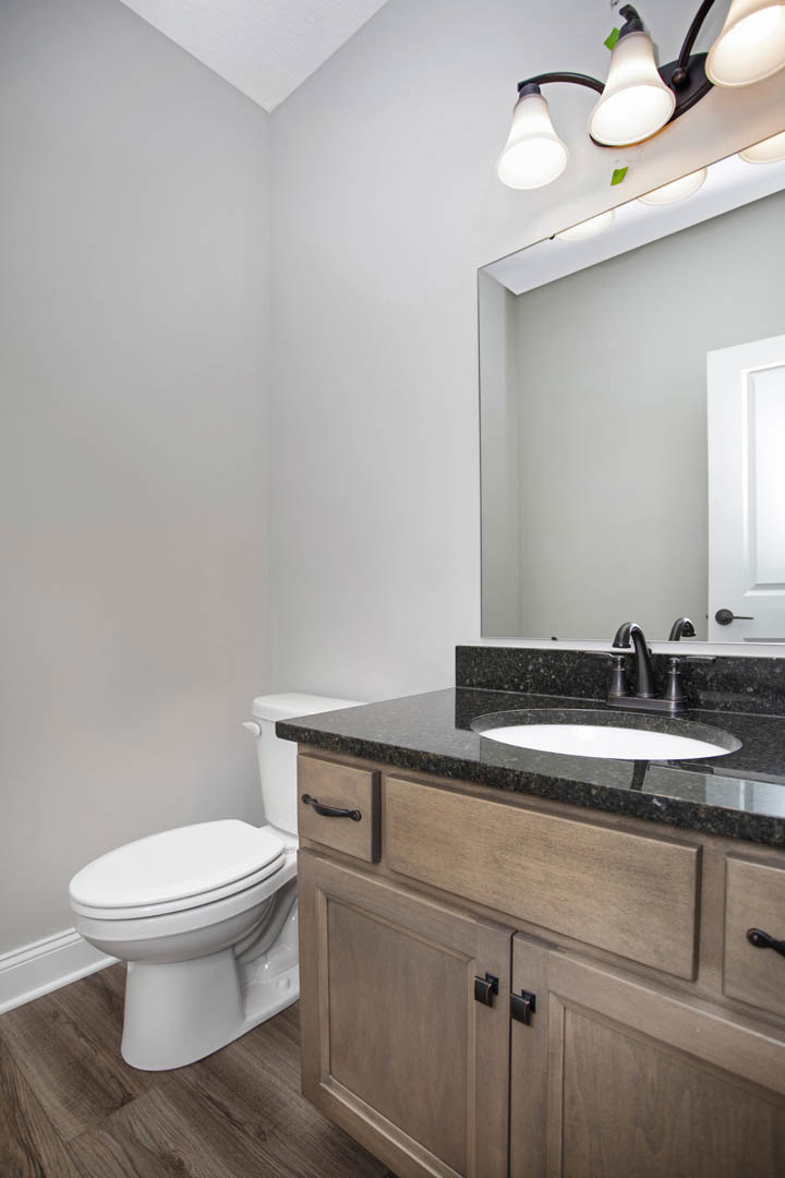 Modern bathroom featuring a white ceramic sink with chrome faucet, adjacent toilet, light gray tile walls, white countertop, and sleek cabinetry