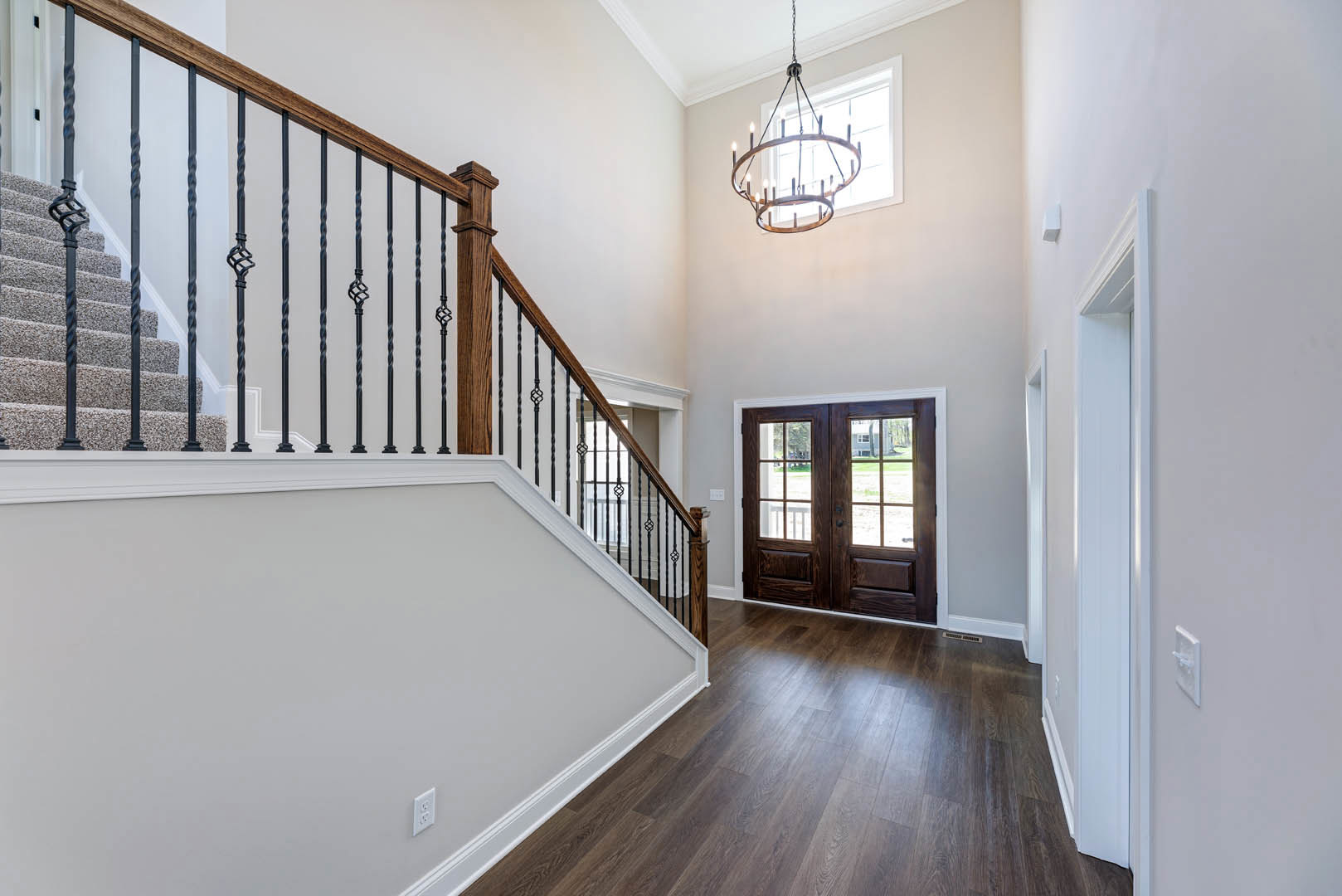 Hallway with hardwood floors, white walls, glass-paneled double doors, wood staircase featuring black metal railings, and ceiling-mounted chandelier