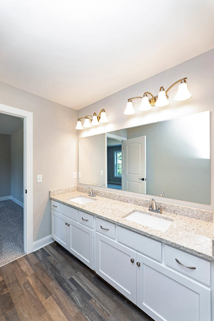 Bathroom with expansive mirror above double sink vanity, white countertop, dark cabinetry, tiled floor, and modern light fixtures.