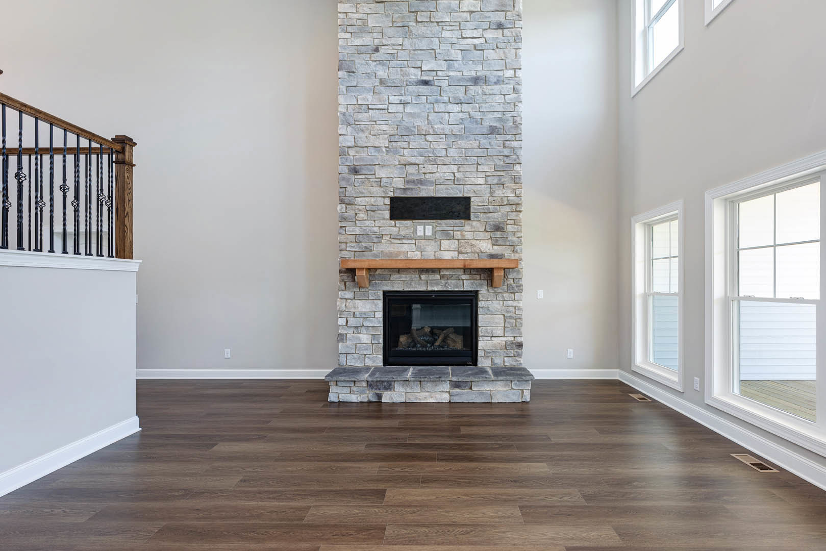 Brick fireplace with stone hearth and wooden mantel, wood flooring, partial view of metal railing, neutral walls