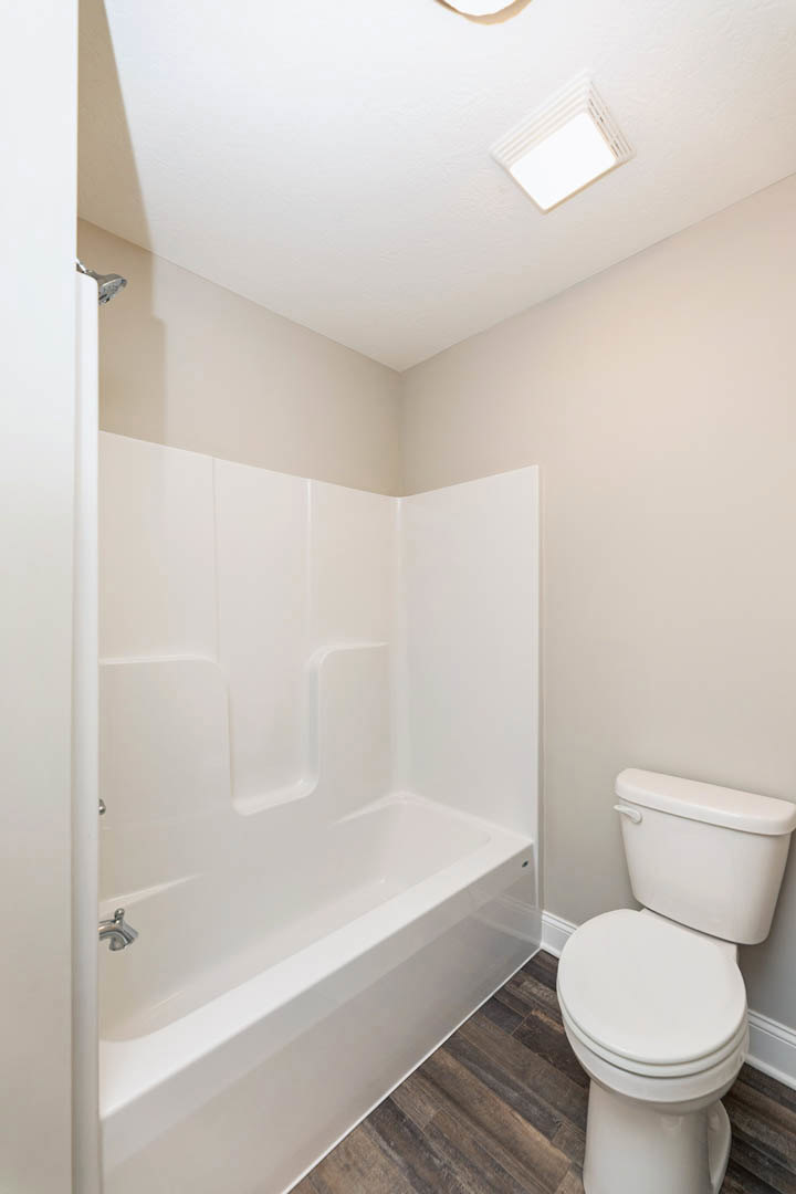 White porcelain toilet and bathtub in a bathroom with light tile flooring and neutral wall finishes