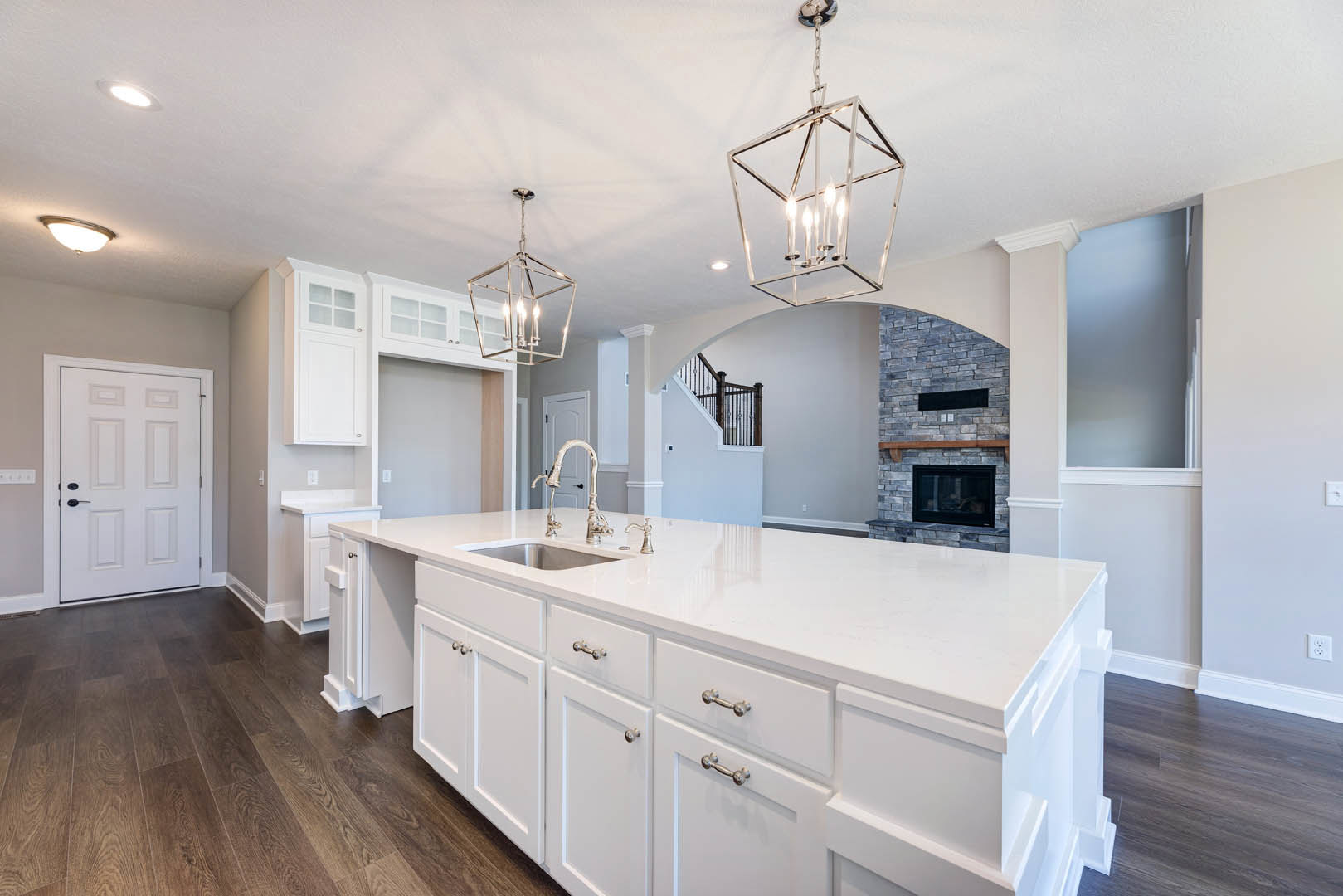 White kitchen with shaker cabinets, large central island with quartz countertop, black hardware on doors and drawers, pendant light fixture above island, hardwood flooring