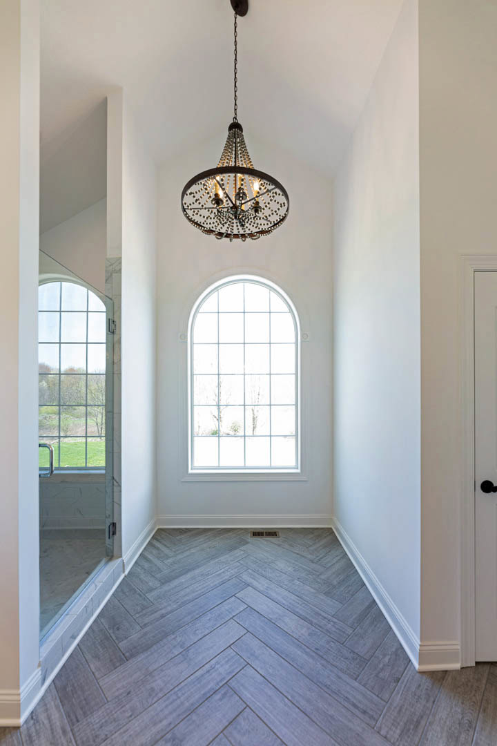 Hallway with wood-patterned laminate flooring, multi-paned window, white walls with molding, and a round chandelier suspended by a chain from the ceiling