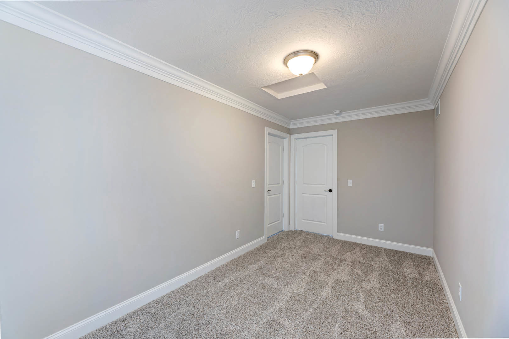 White-walled room with plush beige carpet, black-handled white door, and flush ceiling light fixture