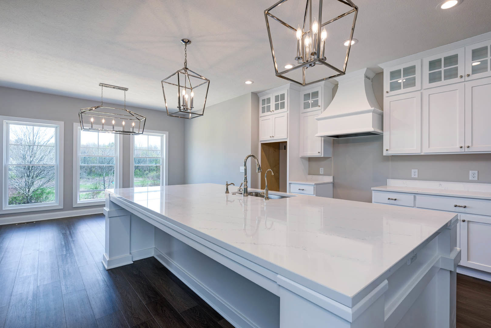 Spacious kitchen featuring a large white island countertop with silver faucets, white cabinetry with glass doors, a close-up chandelier and ceiling light fixture, and a window