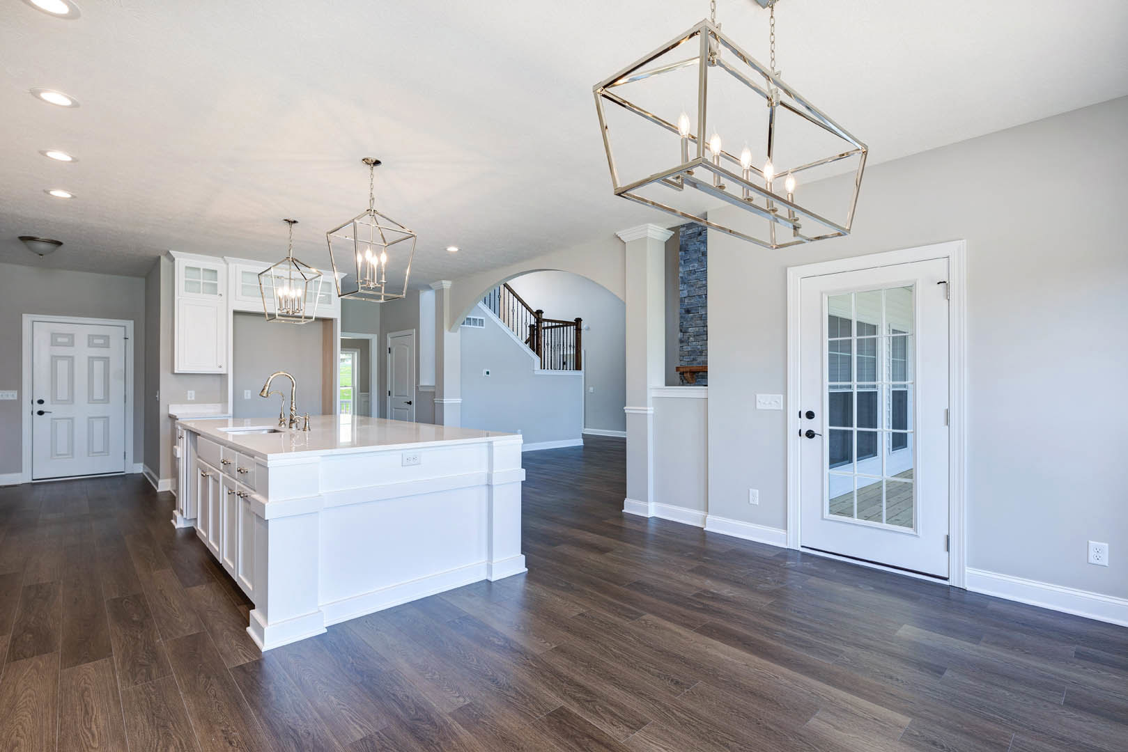 Open kitchen and dining area with hardwood floors, white cabinetry, kitchen island with silver faucet, glass-paneled door, black door handles, and ceiling chandelier.
