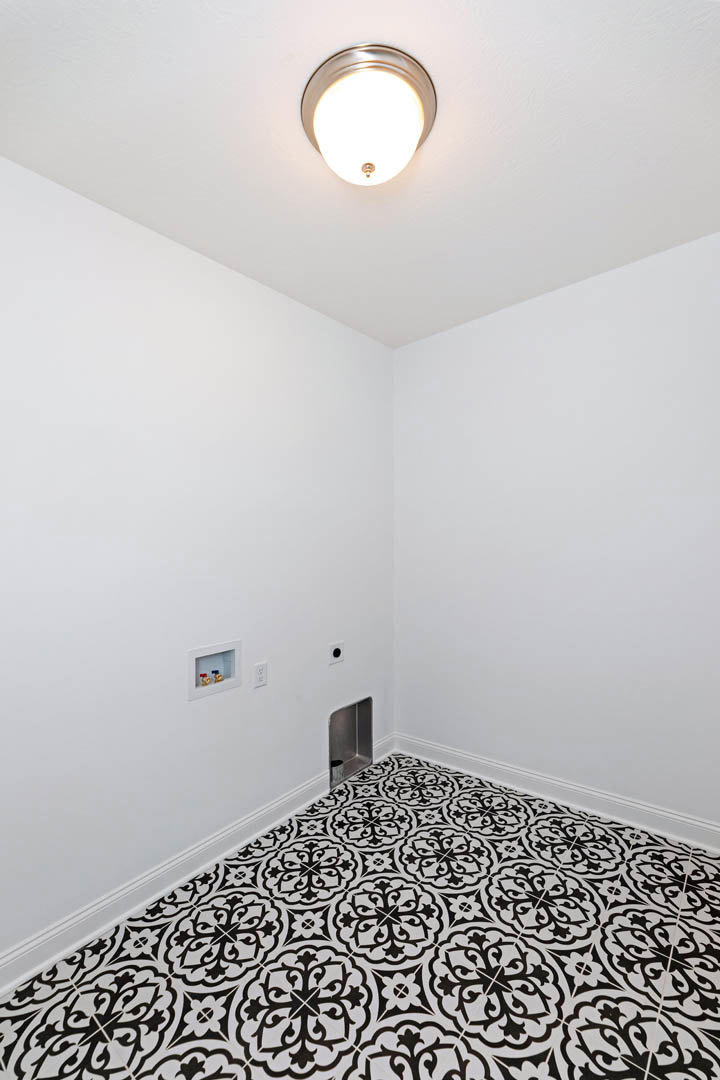 White room featuring a black and white patterned floor, small window on a white plaster wall, ceiling light fixture, and minimal decor.