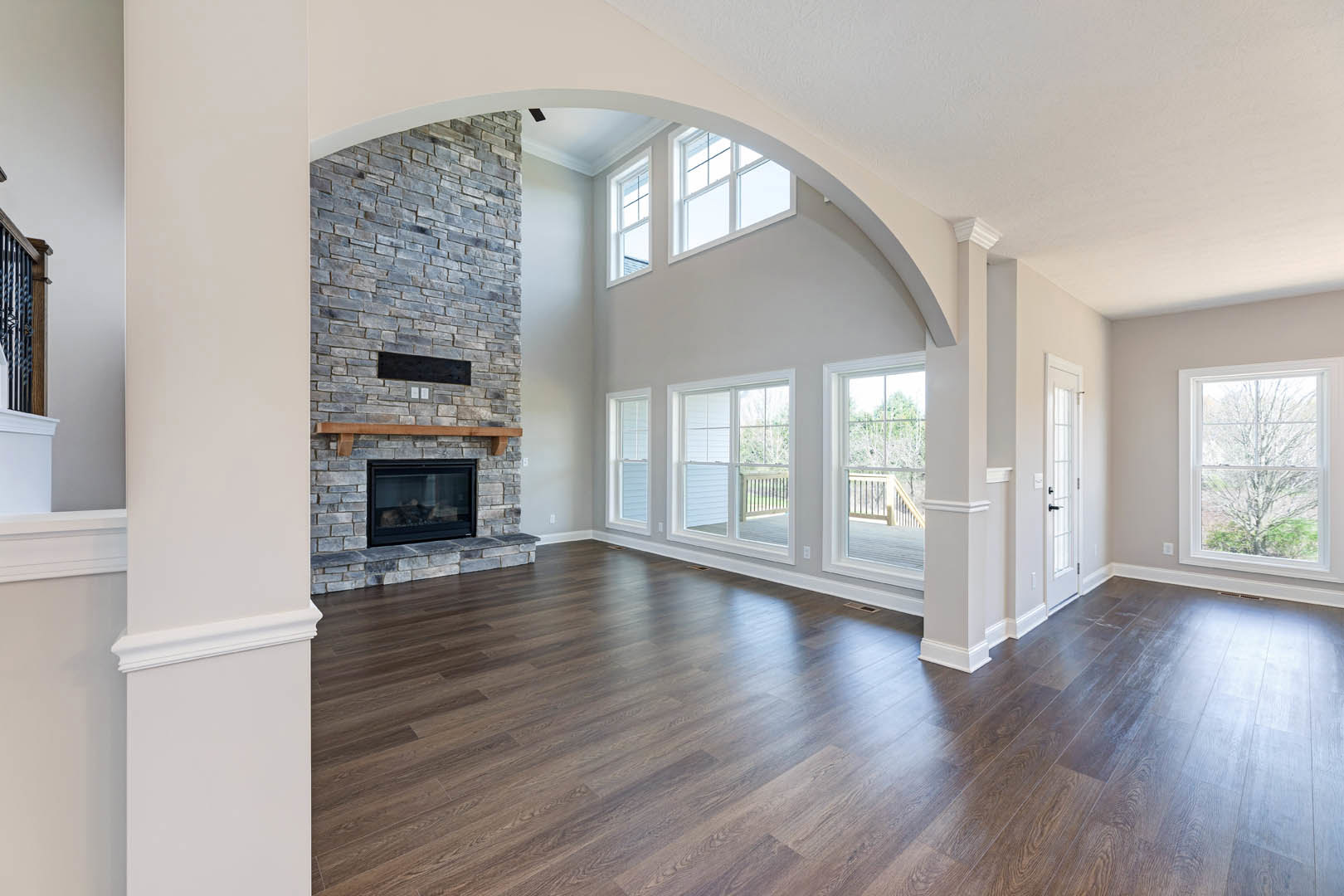 Living room with stone fireplace, glass window showing tree outside, hardwood floor, built-in shelf, and balcony visible through second window