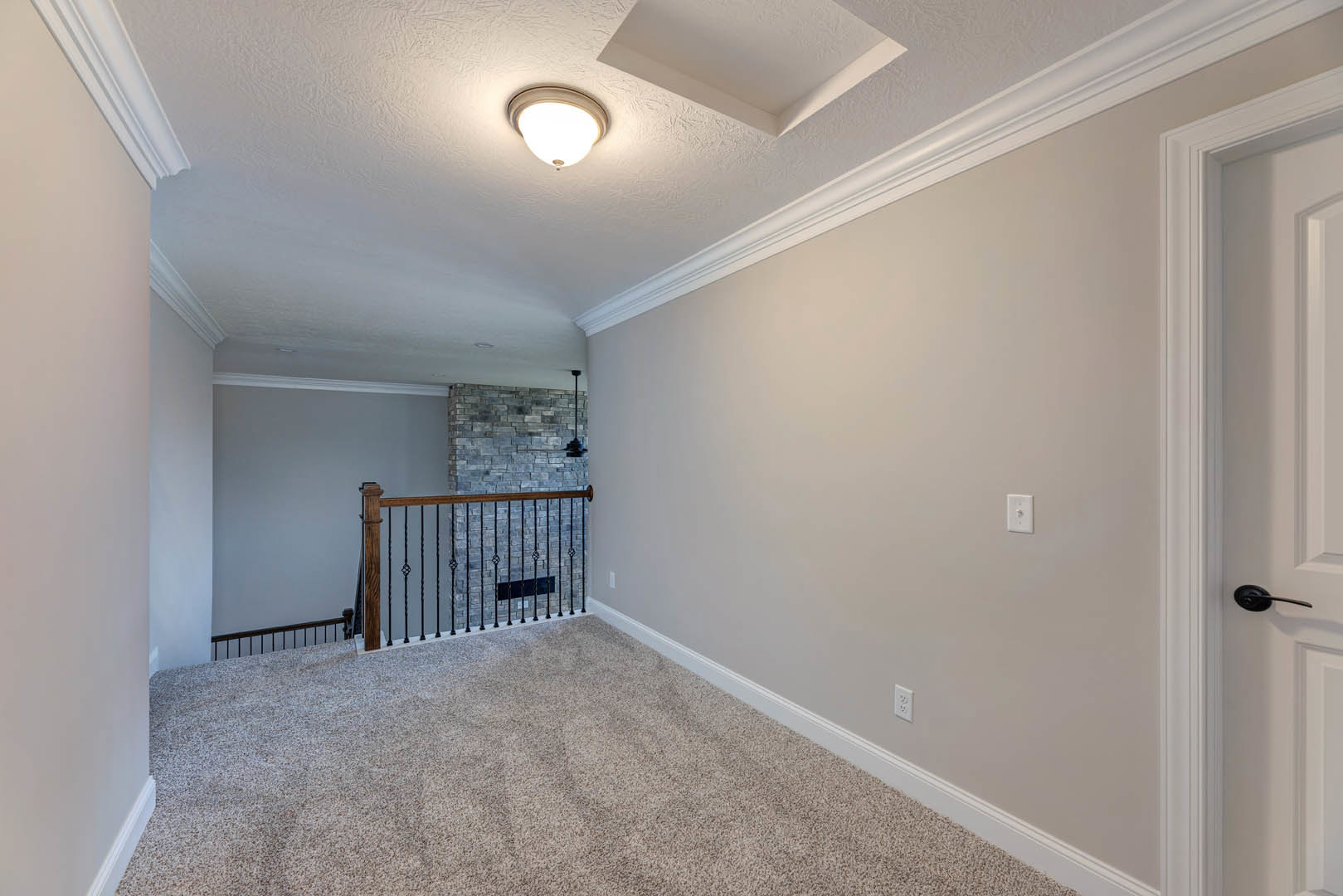 White ceiling with recessed lighting, brushed metal railing, light gray carpet flooring, and smooth plaster walls in a modern interior room.