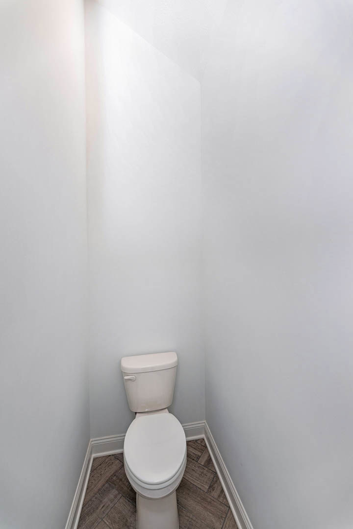 White toilet with closed lid positioned in a tiled bathroom corner, white tank and seat visible against light-colored walls.