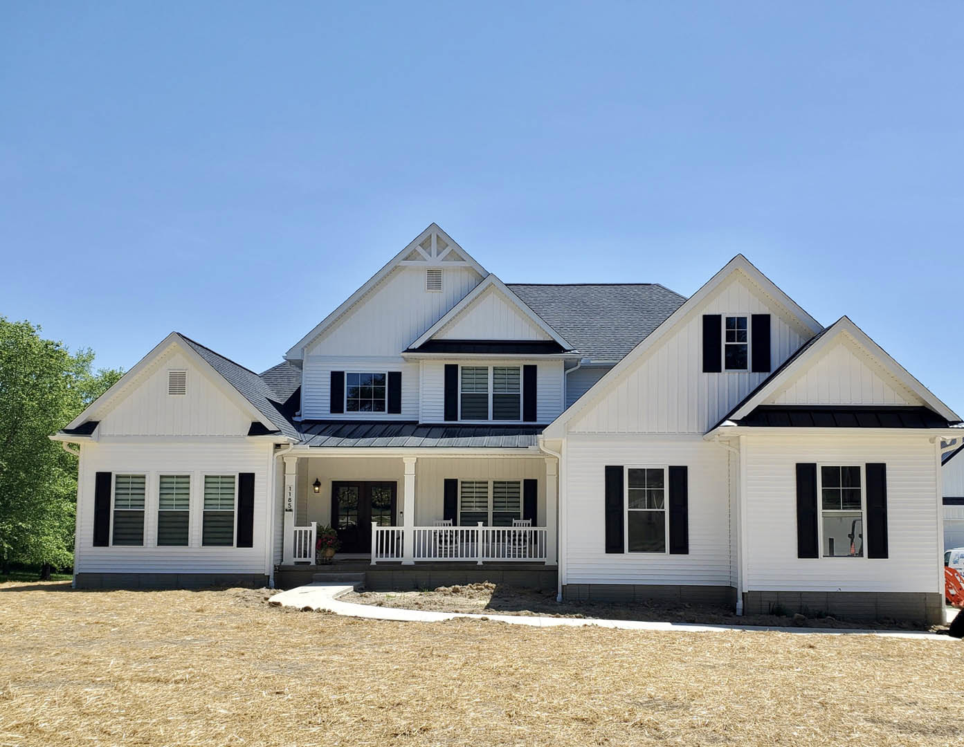 White siding house with black trim and roof, covered front porch with white railing, manicured lawn in foreground, large windows, blue sky above
