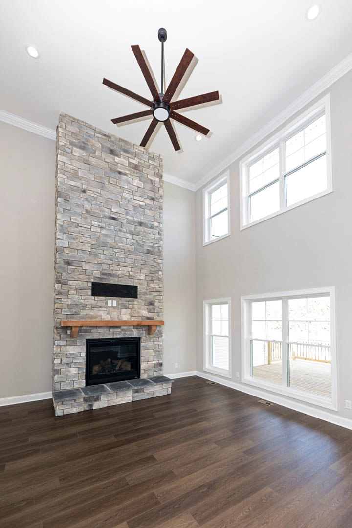 Brick fireplace with glass doors, hardwood flooring, ceiling fan with light, white walls, large window, and wood trim