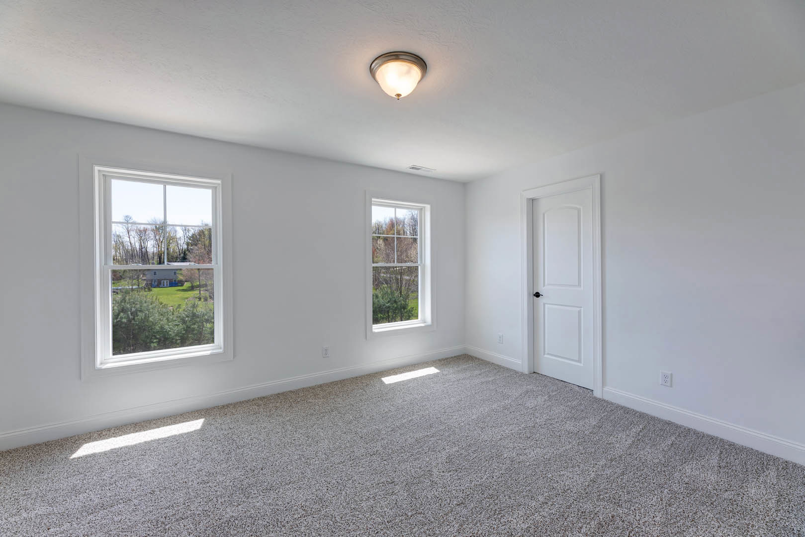 Carpeted room with white walls, white door featuring black handle, ceiling light fixture, large window offering view of green trees