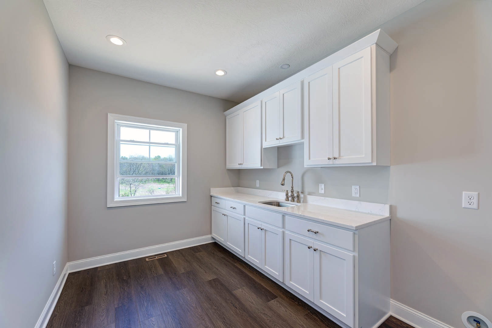 White kitchen cabinets with silver faucet, dark wood floor featuring a vent, window overlooking trees, white electrical outlet on wall