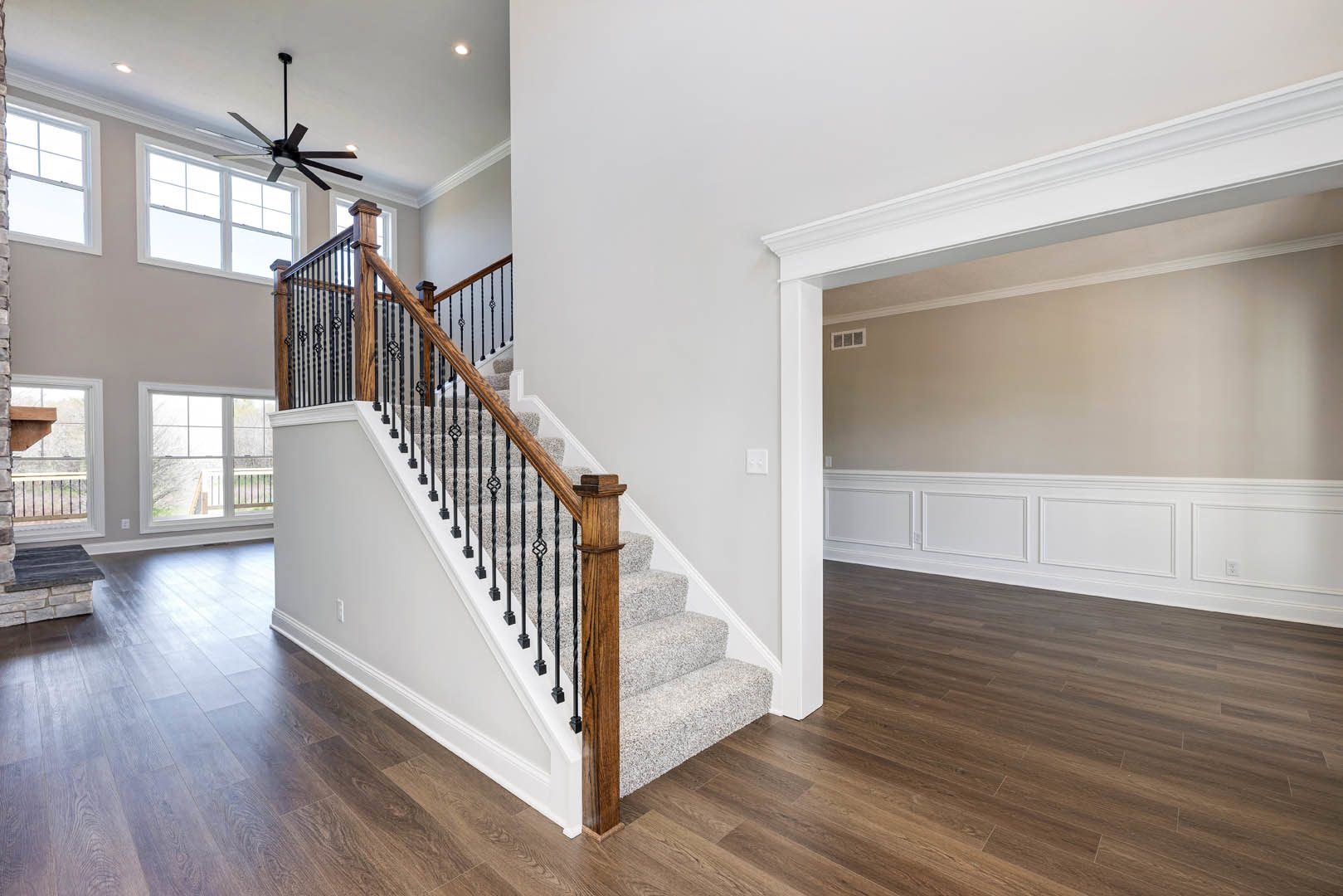 Curved wooden staircase with matching handrail and balusters, laminate wood flooring, ceiling fan with light fixture, window above landing, stone step integrated into brick accent