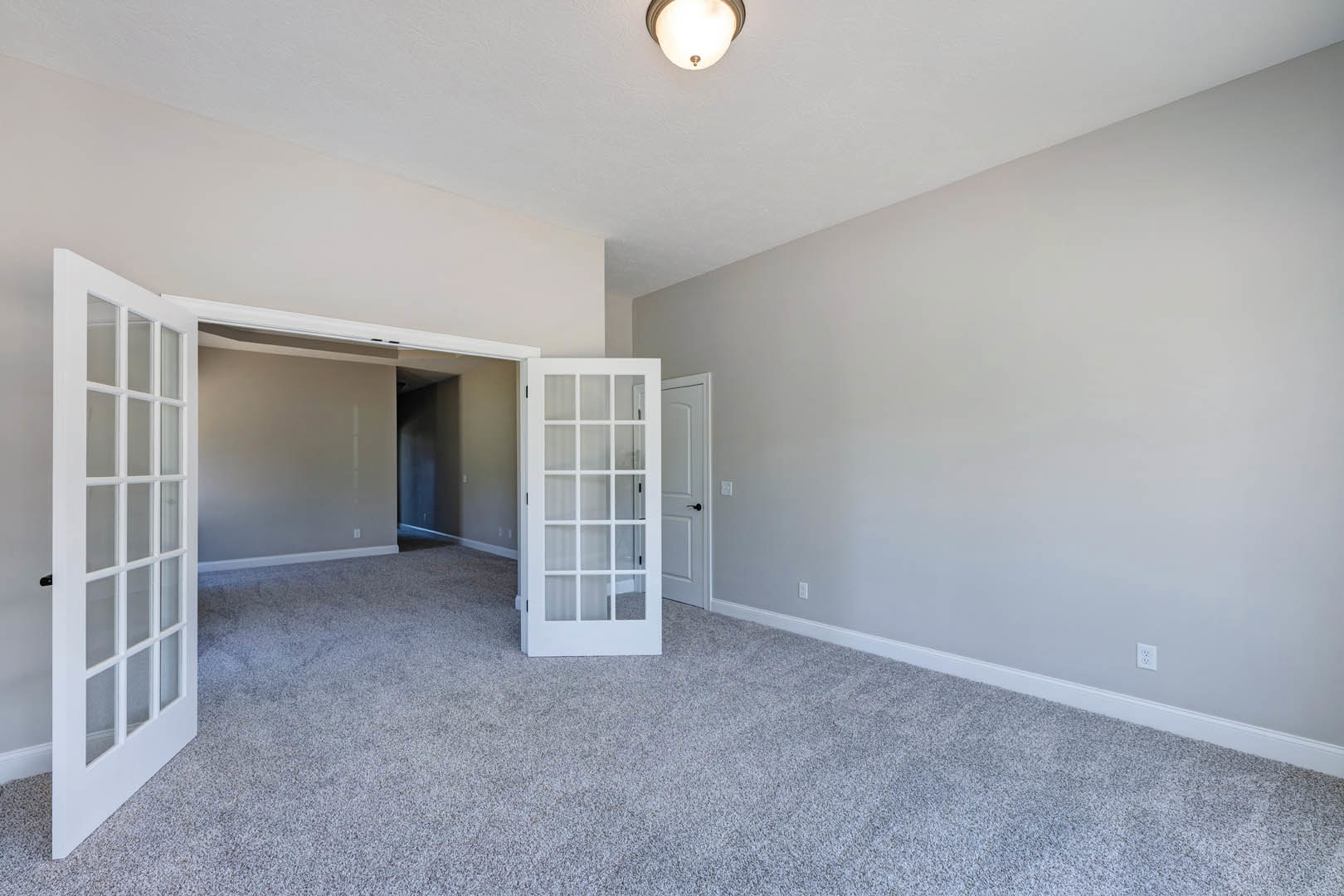 White paneled door with glass panes and black handle opening onto carpeted room with light-colored walls and ceiling